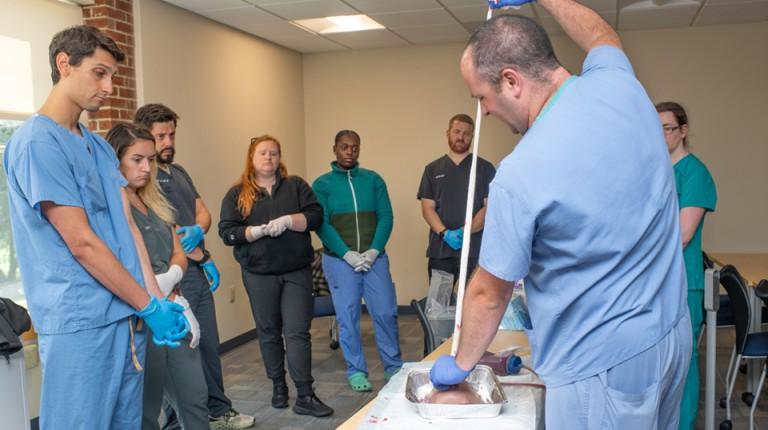 Physician Assistant students watch as their professor demonstrates stopping bleeding